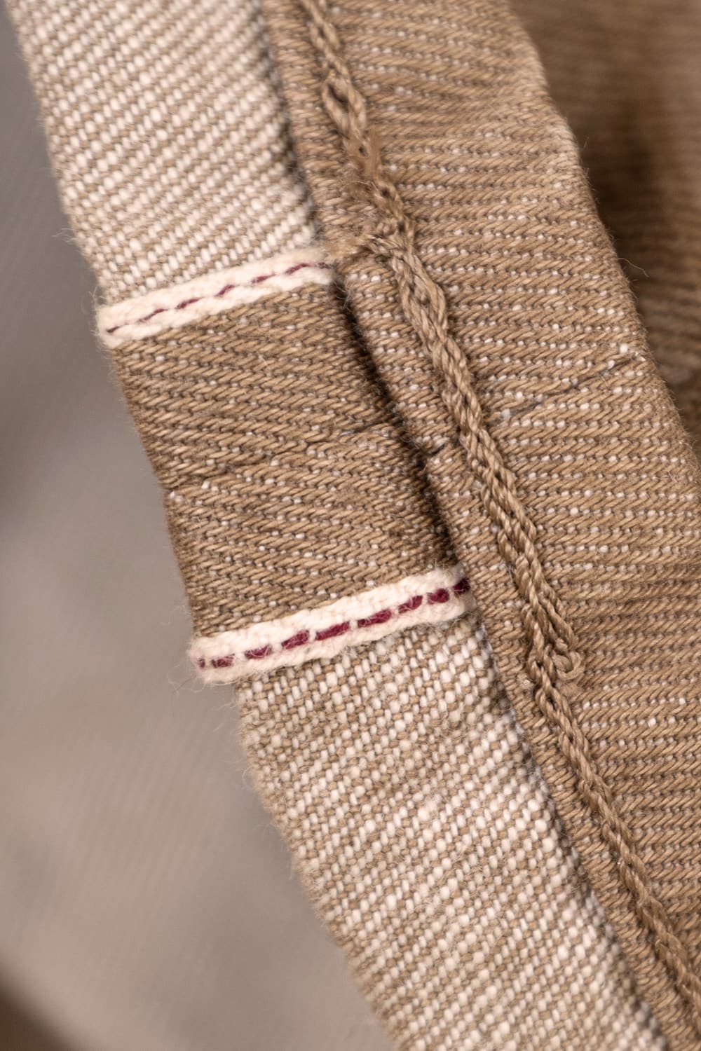 Close-up of a woven textile showing a beige and brown fabric with white and red contrast stitching.