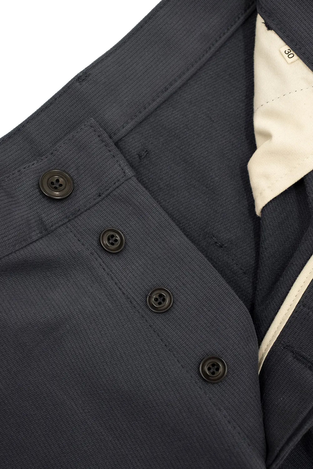 Close-up of a dark navy textured fabric garment with three dark buttons and a cream-colored inner lining visible on the right side.