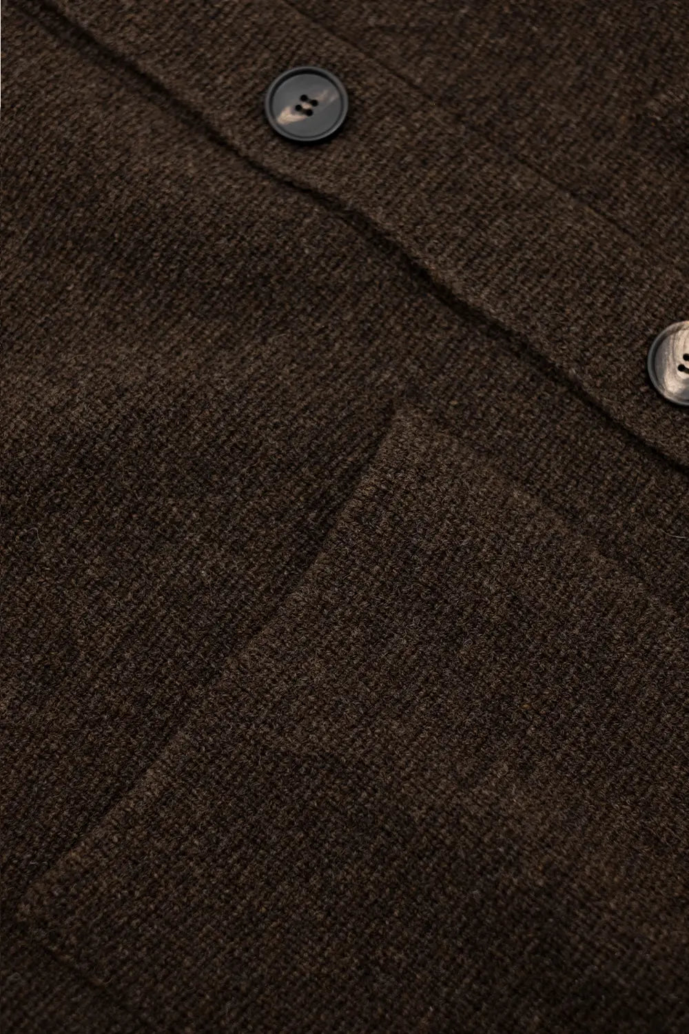 Close-up of a dark brown textured knit fabric with a buttoned collar and a pocket, showing the weave and button details.