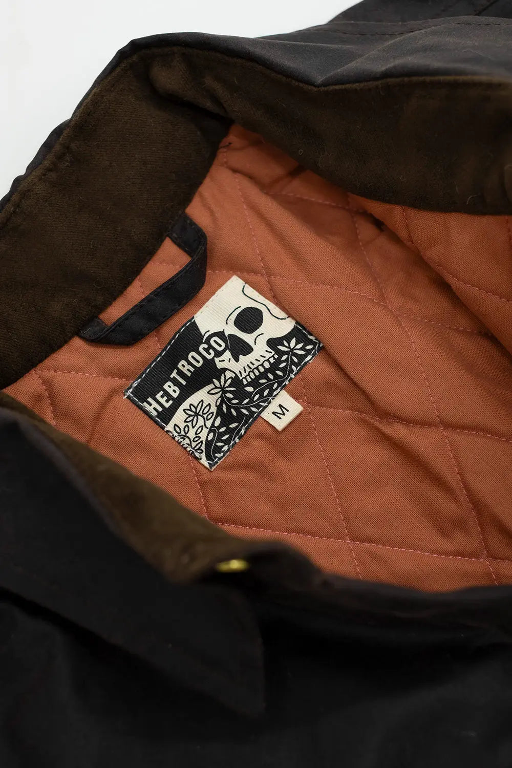 Close-up of the interior of a dark brown jacket or overshirt, showing a quilted rust-orange lining and a sewn-in label that reads Westrock with a skull logo.