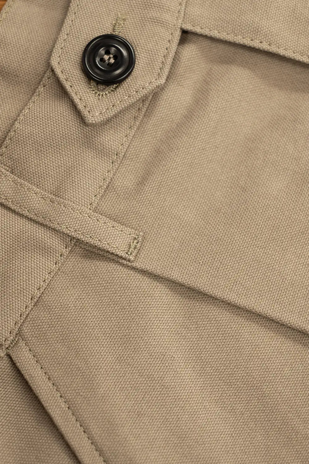 Close-up of a beige woven fabric garment detail with a black button and stitched pocket construction.