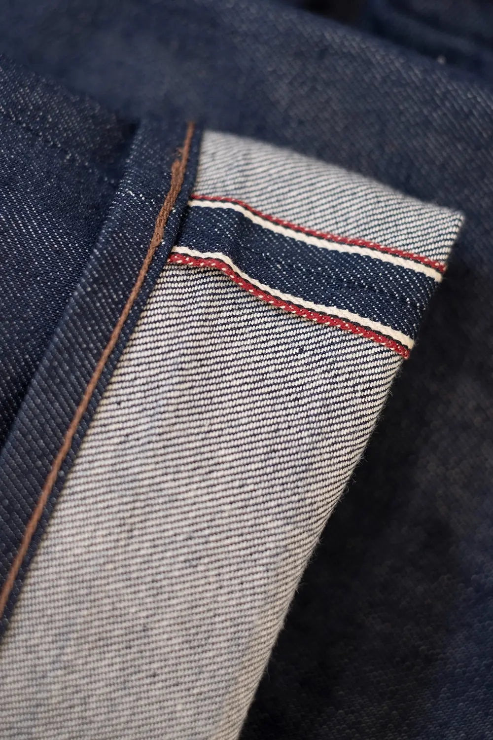 Close-up of a folded pair of dark indigo denim jeans showing the lighter gray heathered inner fabric with red and white contrast stitching.