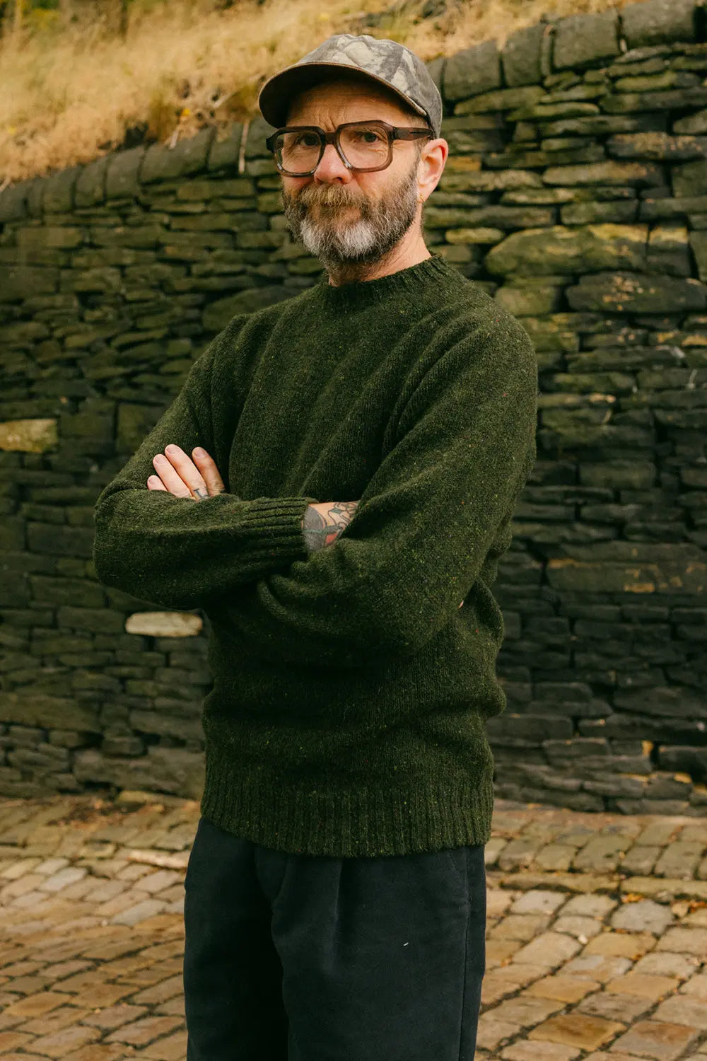 Ed stood crossed arms with the tod ned jumper on in front of a dry stone wall
