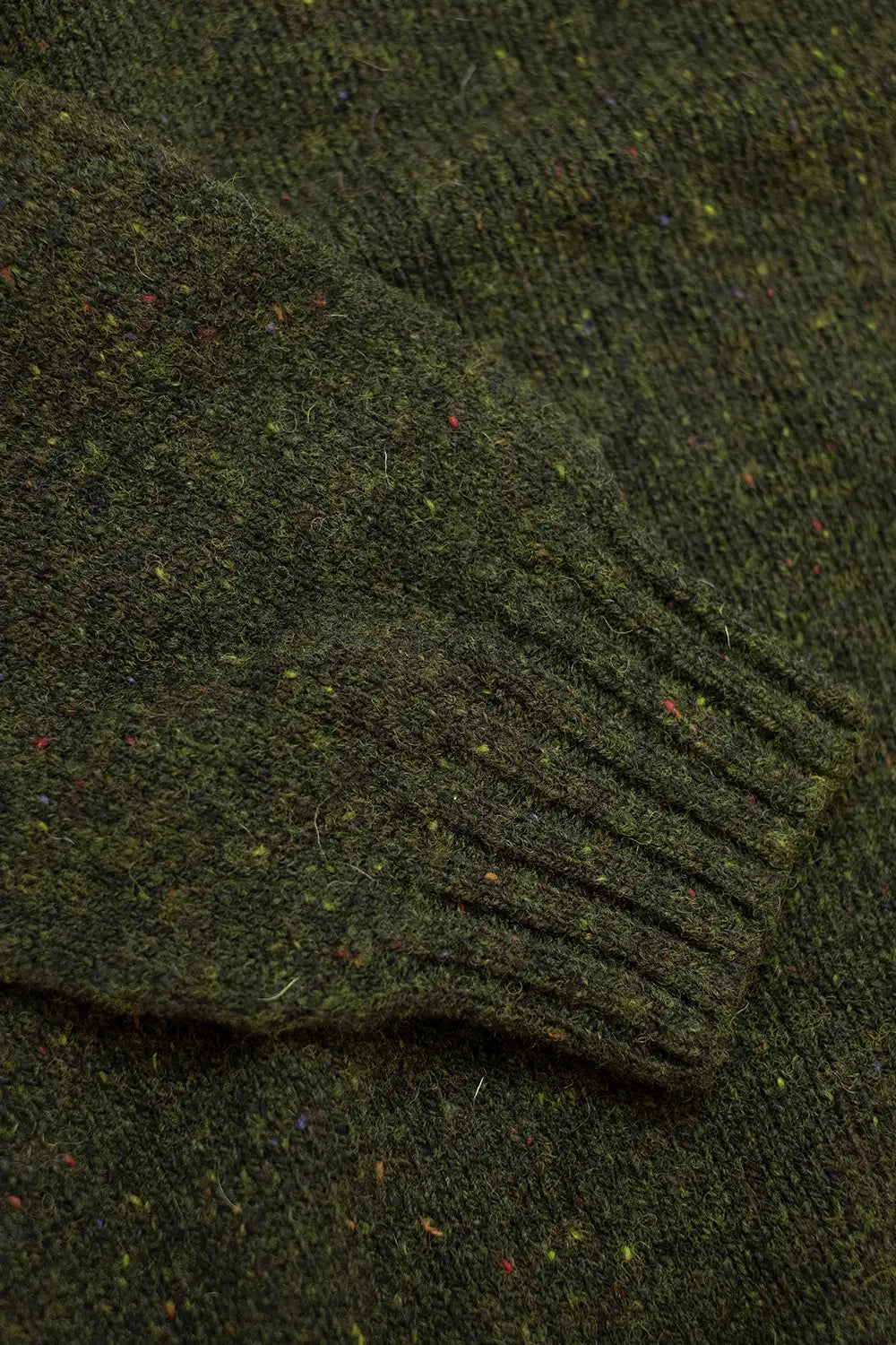 Close-up of a dark olive green knit fabric with a ribbed cuff and small multicolored flecks throughout.