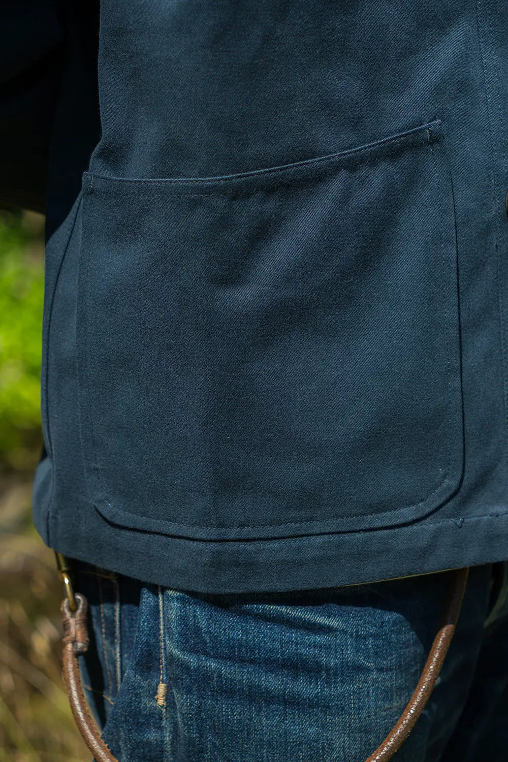 Close-up of a dark navy blue canvas utility vest with a large front patch pocket, worn over blue jeans.