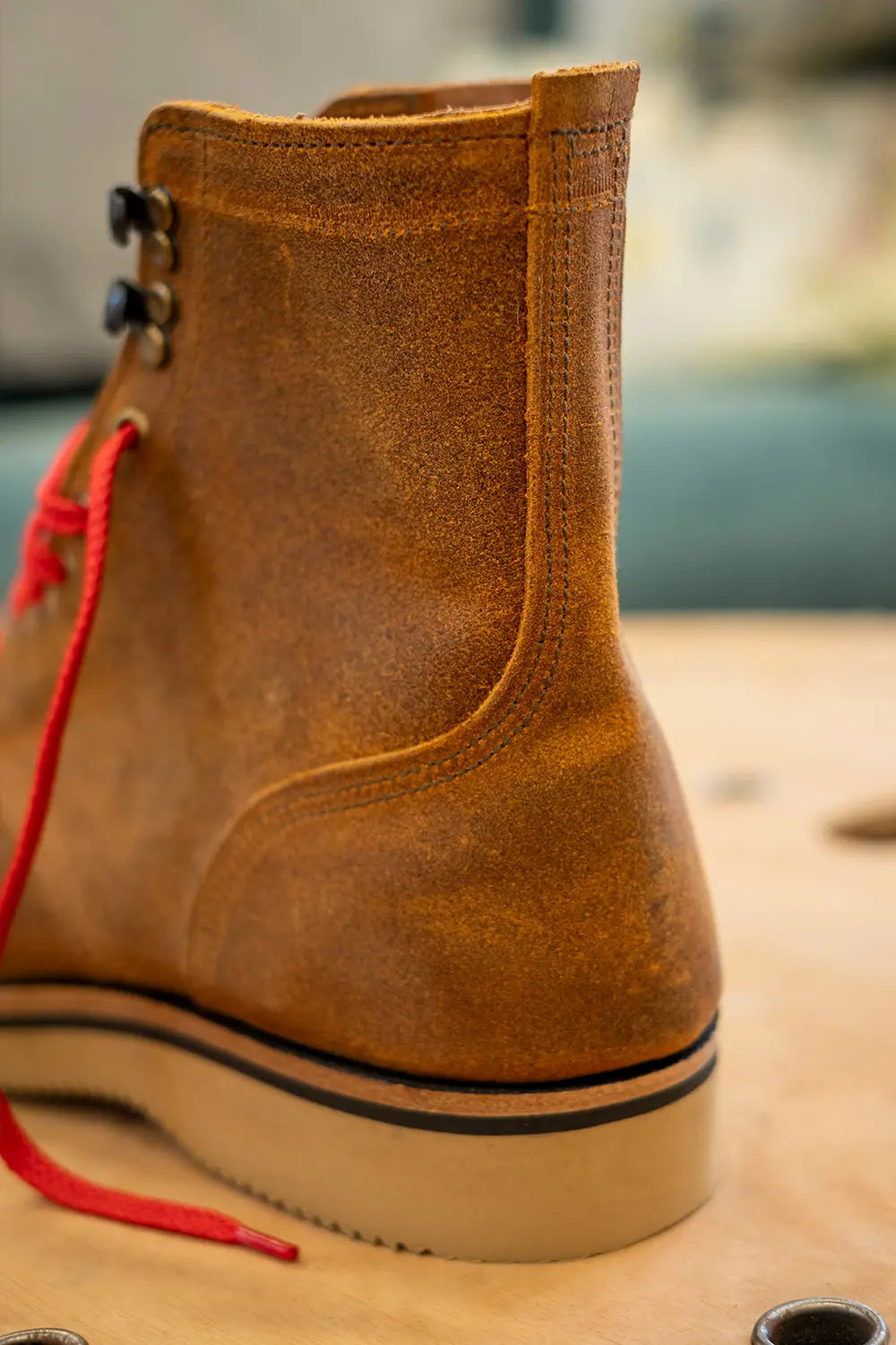 A close-up of a brown suede ankle boot with red laces and a thick beige sole, resting on a wooden surface.