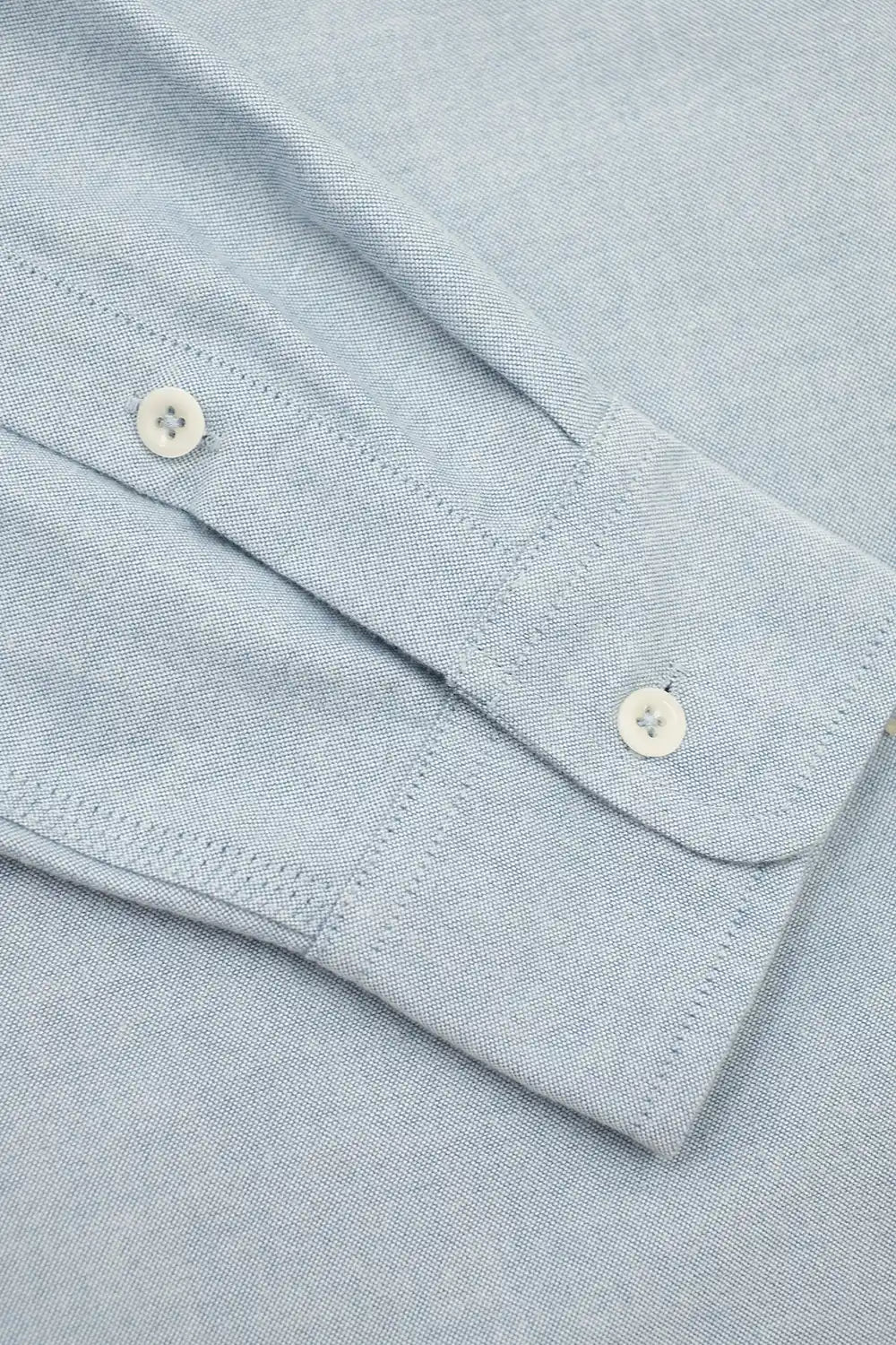 Close-up of a light blue knit fabric sleeve showing the buttoned cuff and fine stitching.