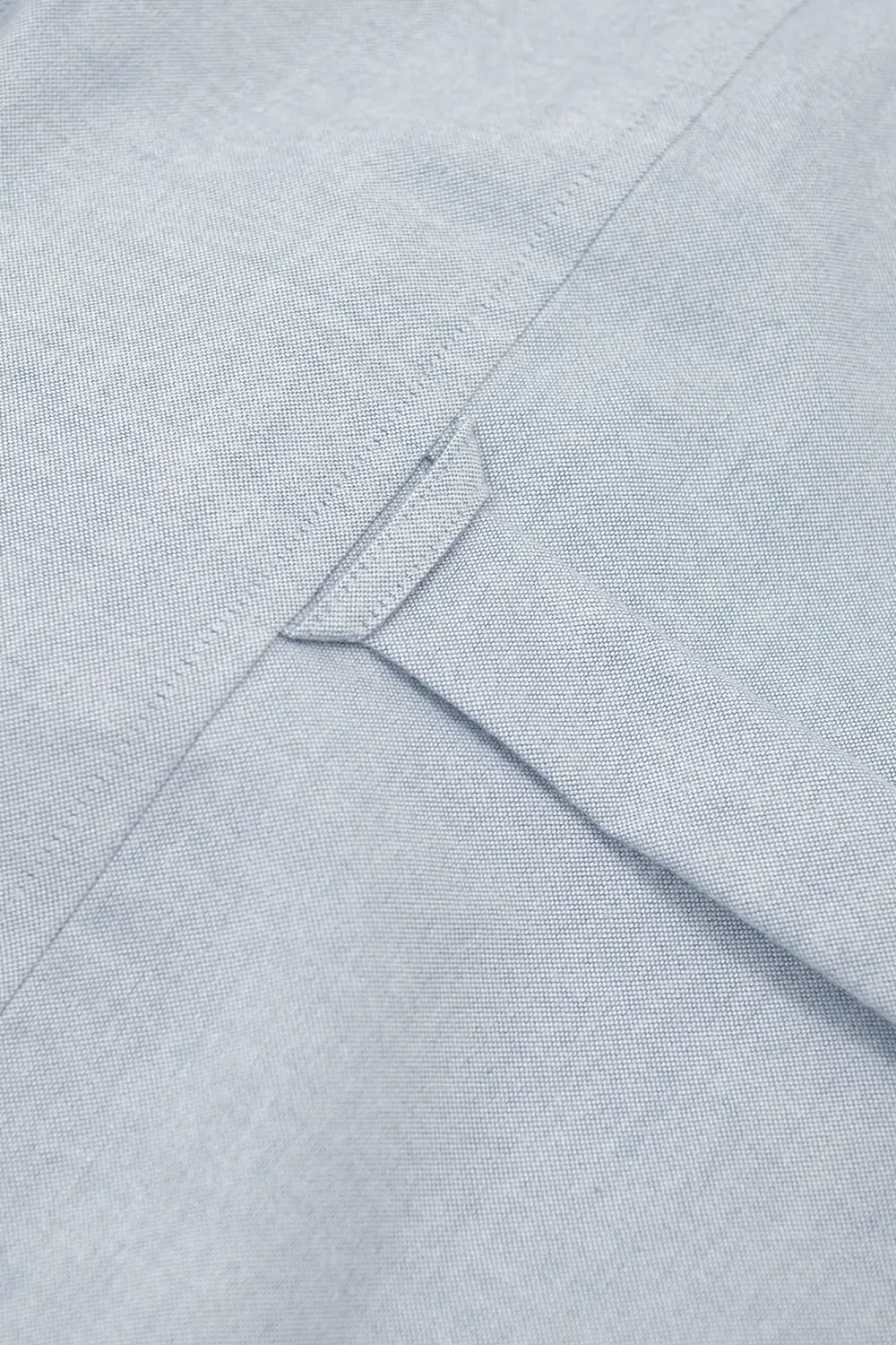 Close-up of a light blue-gray textured fabric with a small stitched tab detail.