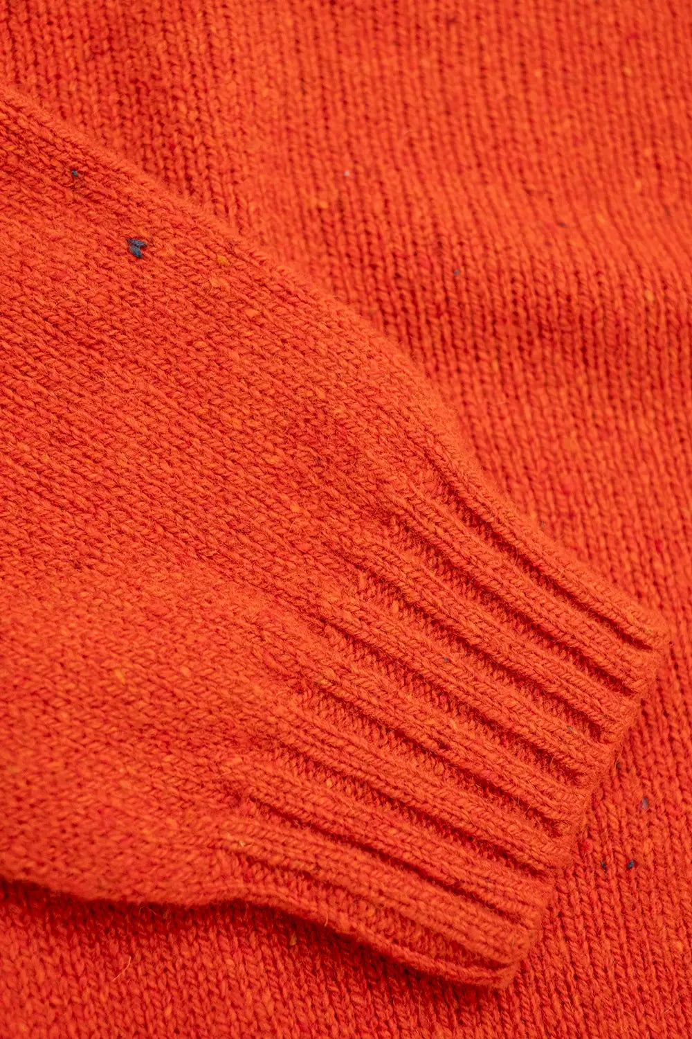Close-up of a textured knit jumper in a vibrant burnt orange color, showing the ribbed cuff detail.
