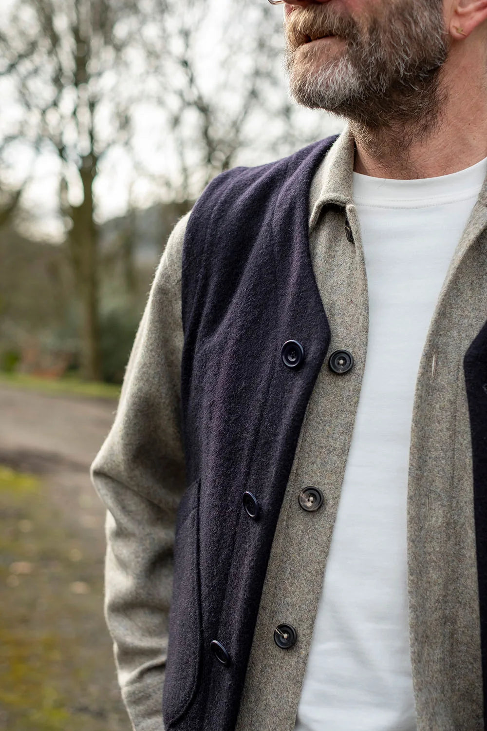 A close-up of a man outdoors wearing a dark navy wool vest over a wool overshirt.