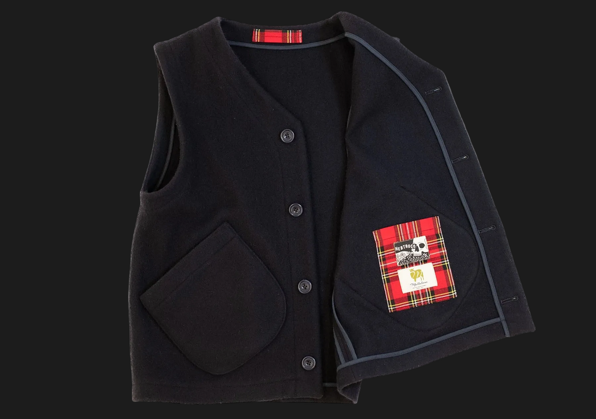 A navy wool vest with a red tartan plaid patch pocket on the left side, featuring a button closure and a small brand label.