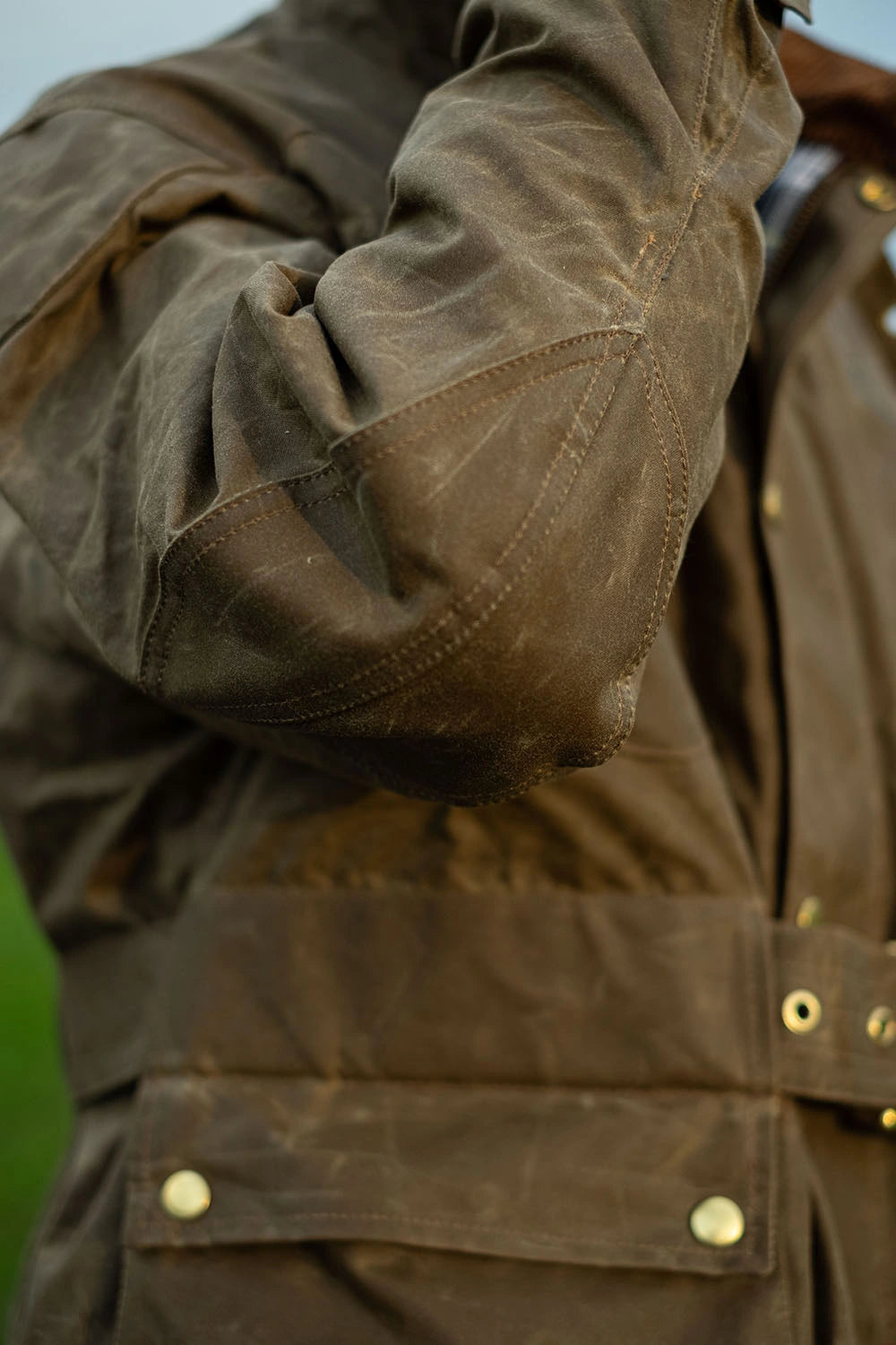 Close-up of a brown waxed canvas jacket with brass snap buttons and a textured, weathered finish.