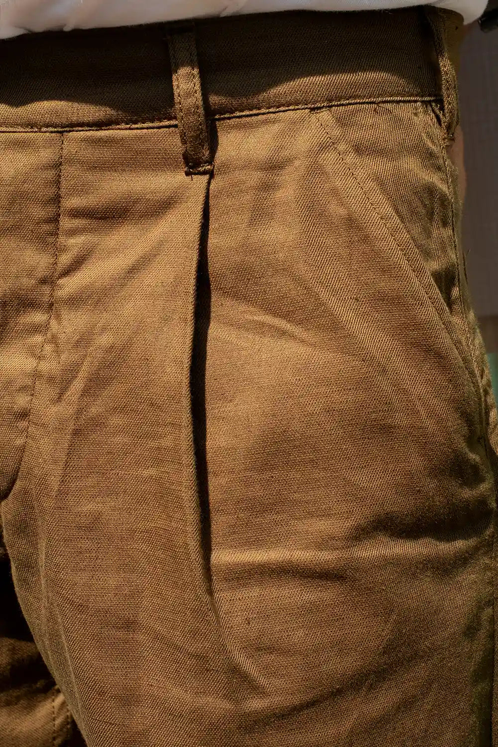 Close-up of brown trousers showing the fabric texture, waistband, belt loops, and front pleat detail.