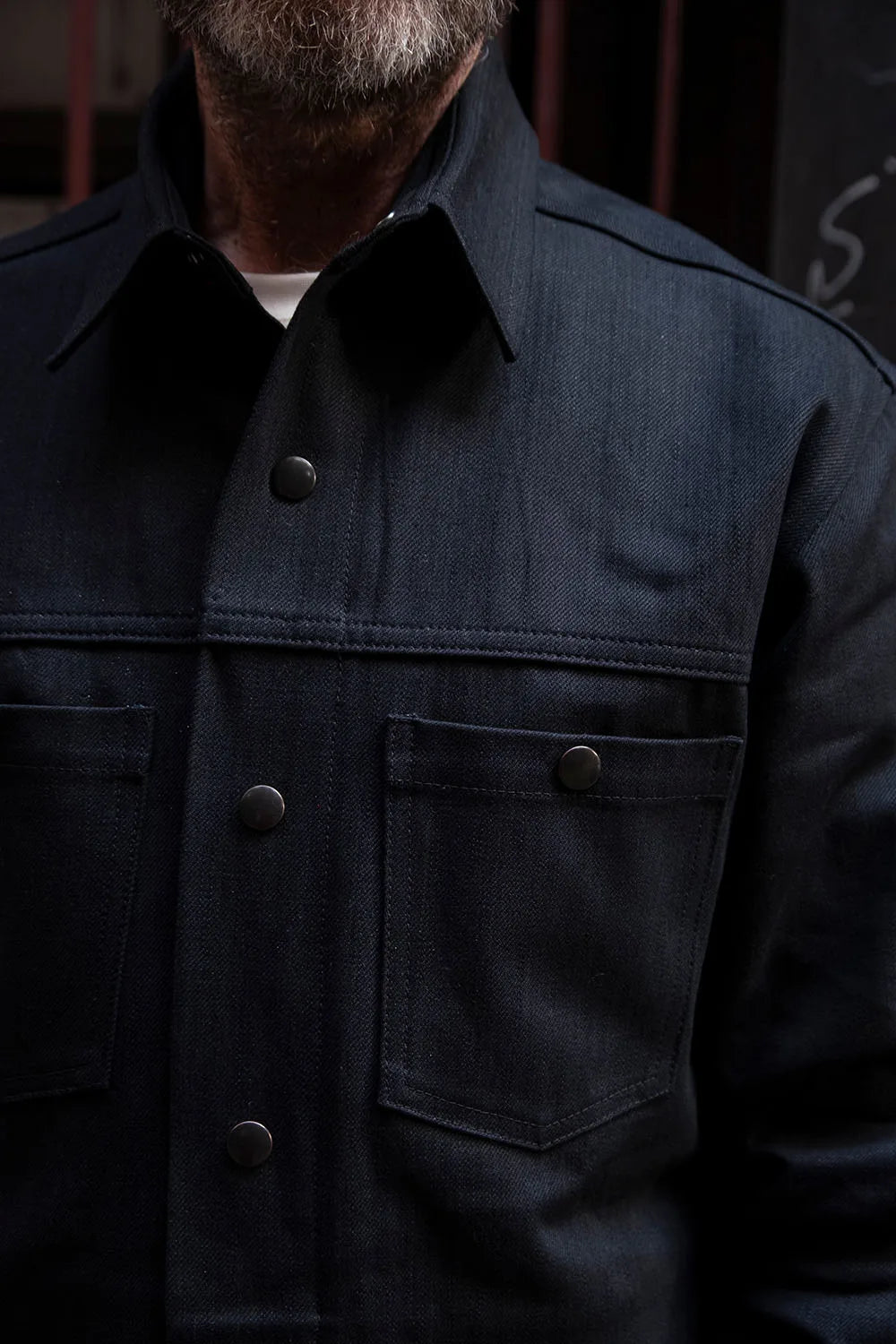 Close-up of Ed wearing a pitch black ironshirt with dark metal buttons and a classic collar.
