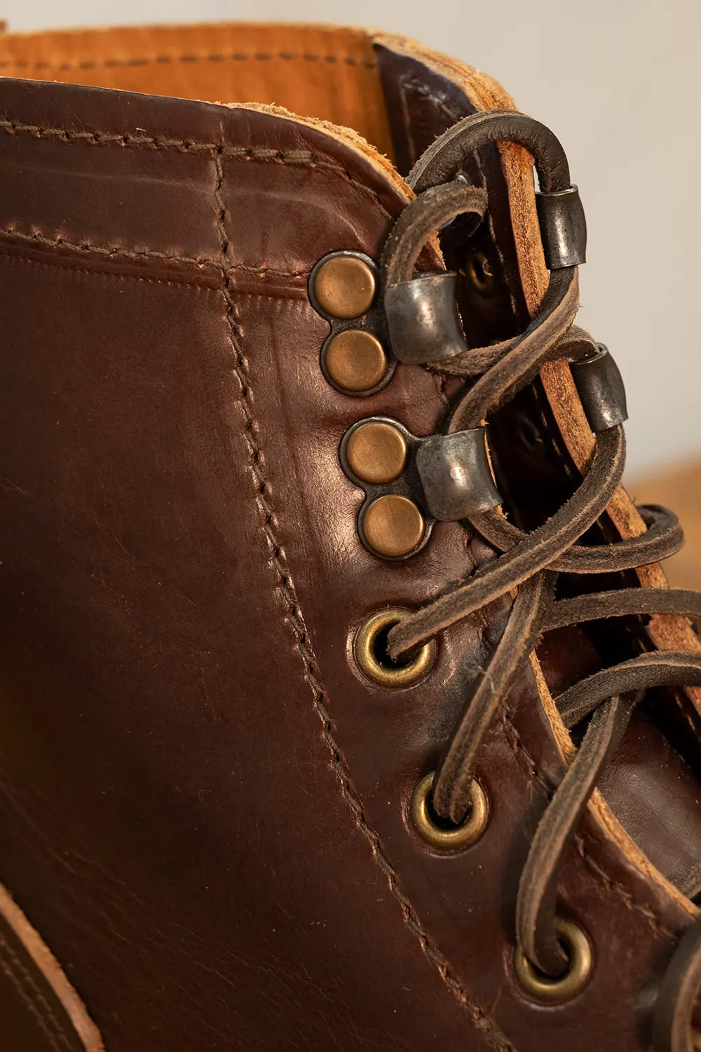 Close-up of a dark brown leather lace-up boot showing the side eyelets, laces, and stitching details.