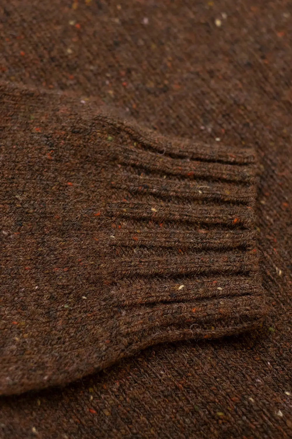 Close-up of a dark brown ribbed knit cuff with flecks of lighter threads, set against a matching textured brown fabric background.