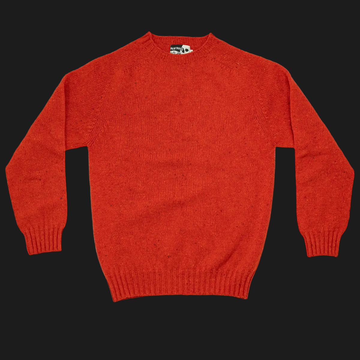 A bright orange-red knit crewneck sweater laid flat against a solid black background. The sweater has long sleeves with ribbed cuffs, a ribbed hem, and a small visible neck label.