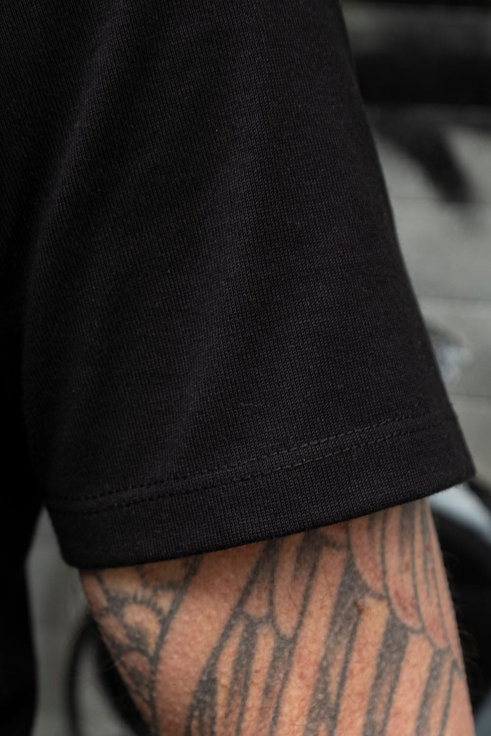 Close-up of a person's tattooed forearm wearing a black short-sleeve knit top, showing the ribbed cuff and sleeve hem.