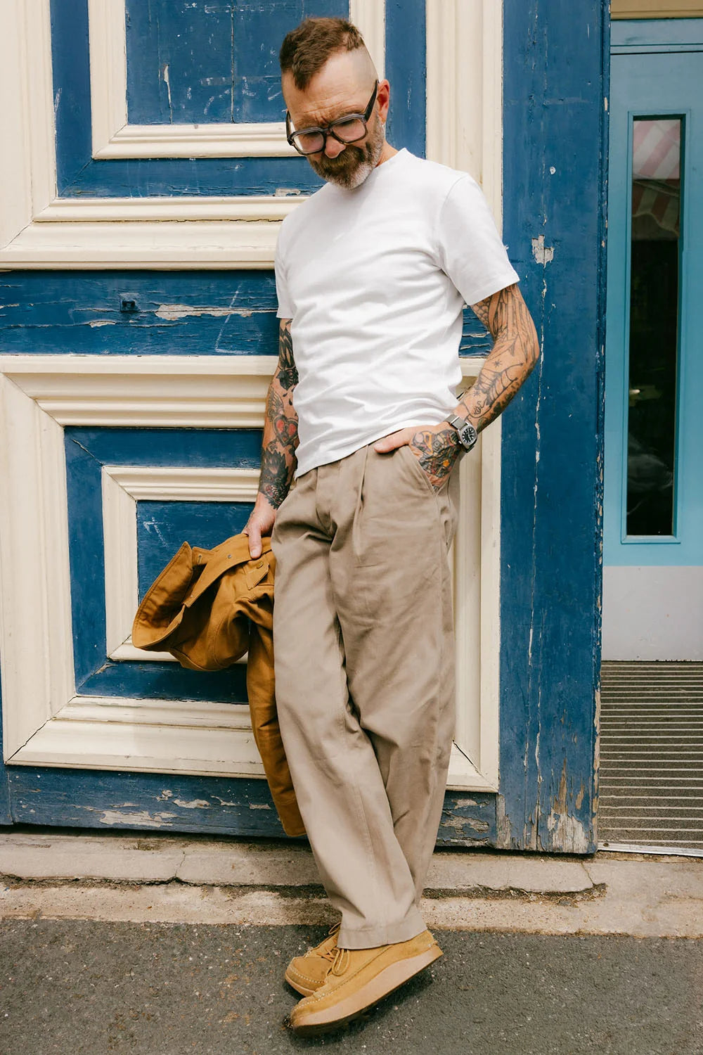 Man wearing a white t-shirt and beige pants standing in front of a blue door.