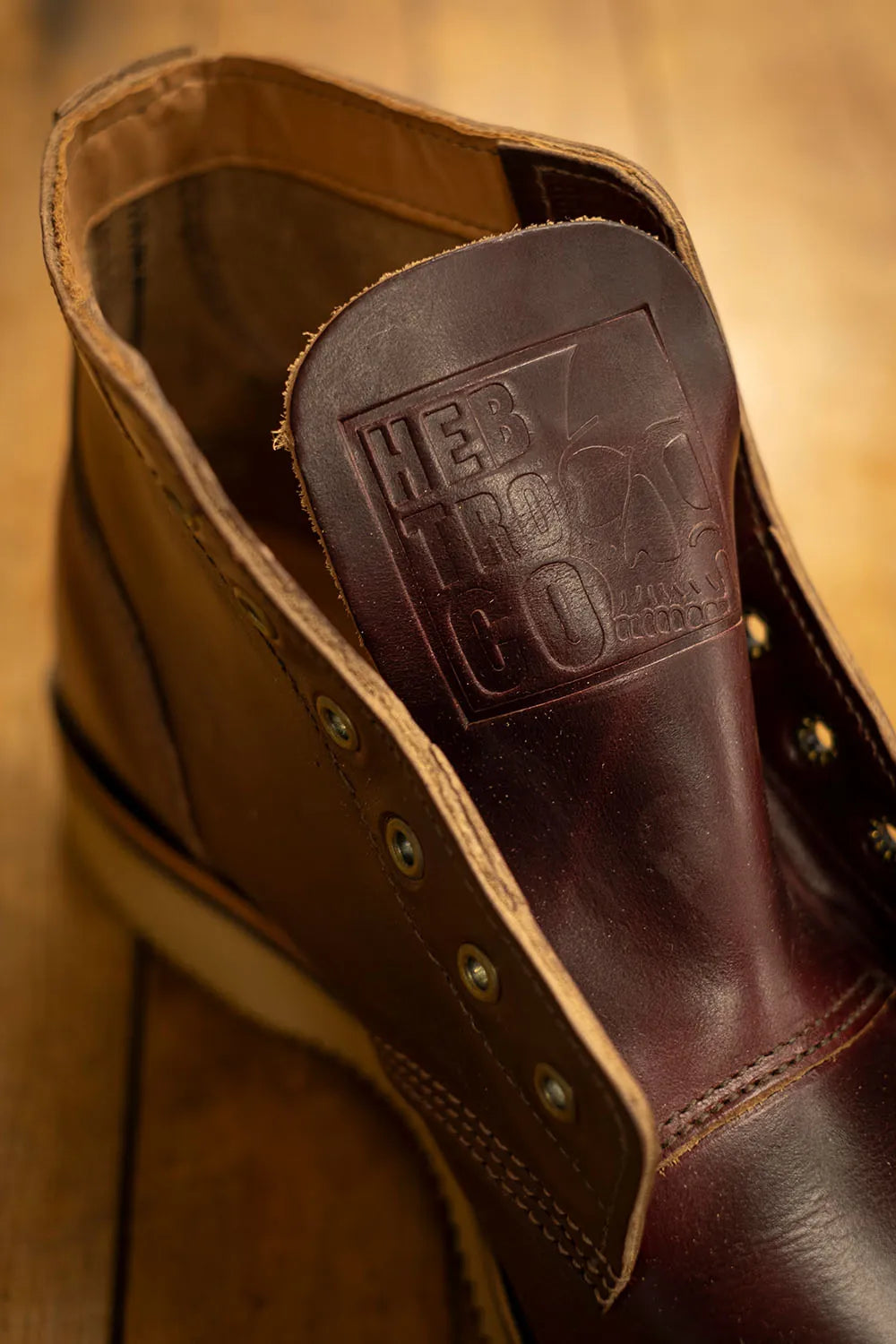 A close-up of a brown leather lace-up boot with a dark brown embossed heel patch reading HEBTROCO.