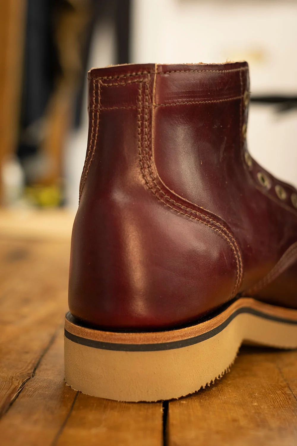 A close-up shot of the back heel of a dark reddish-brown leather ankle boot resting on a wooden floor.