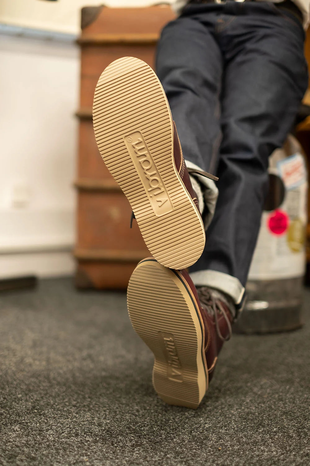 A person wearing dark brown leather boots with tan rubber soles, shown from behind as they kick up one boot. The brand name 'VINTA' is embossed on the sole.