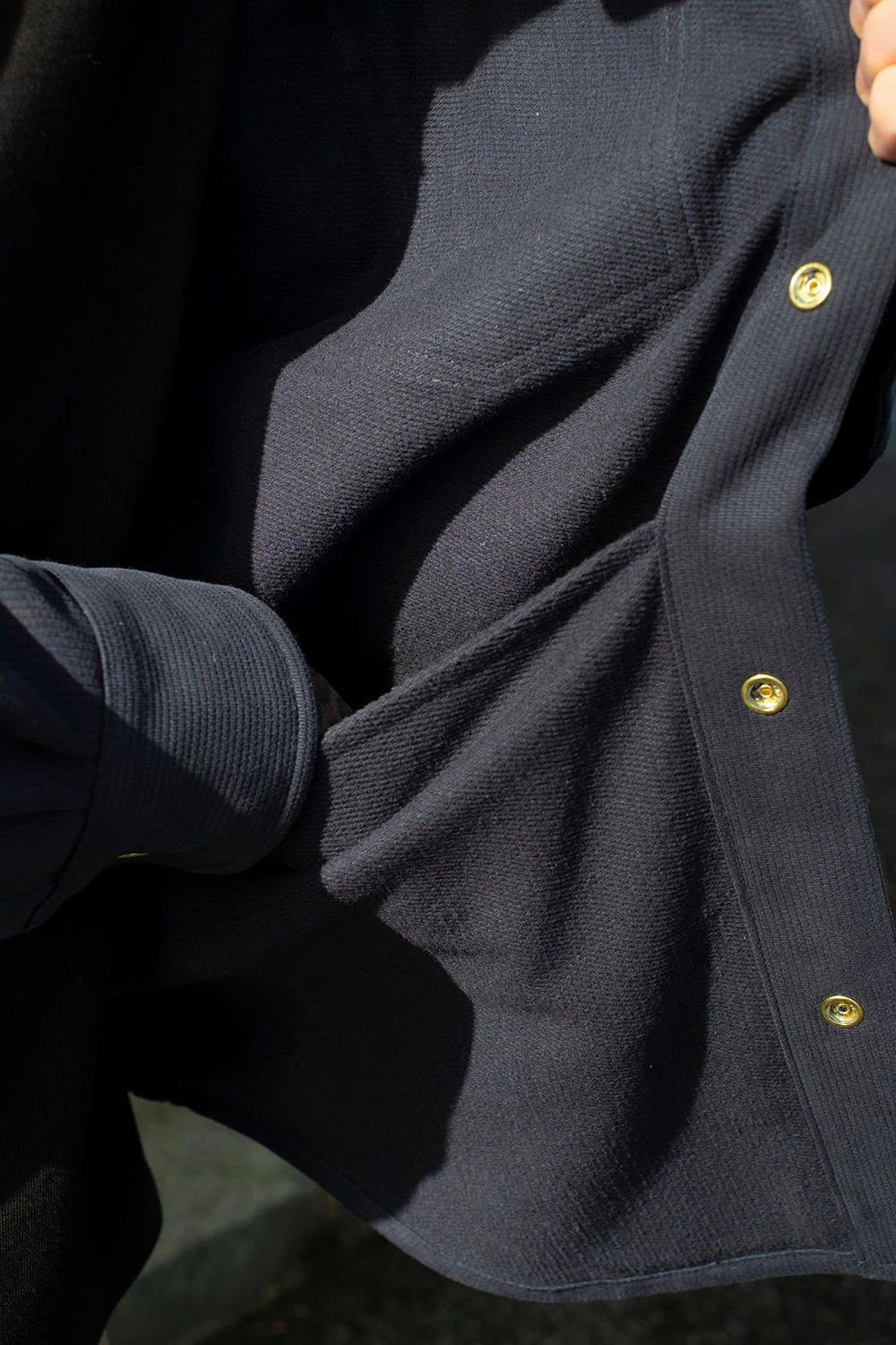 Close-up of a navy bedford cord iron shirt, being worn by a person whose hand is visible at the top right.