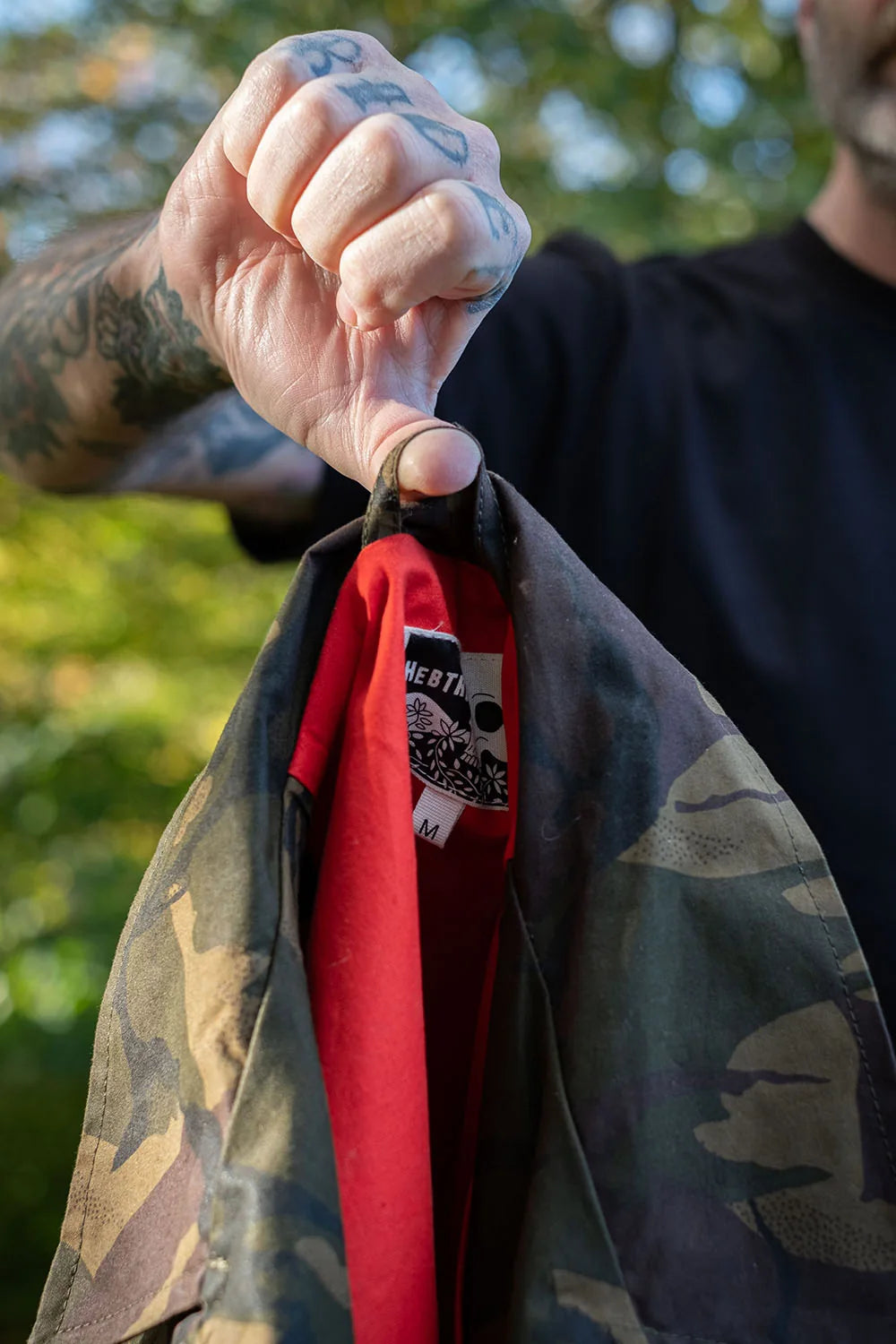 Ed holds the jacksnipe crosshair jacket up by its coat hook showing the red lining and the hebtroco logo