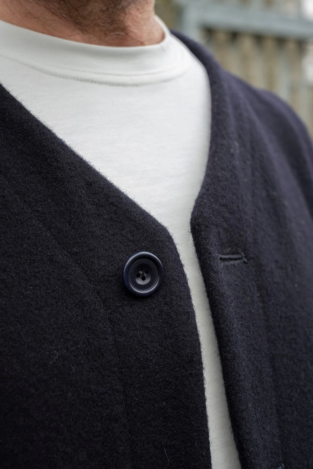 Close-up of a person wearing a navy melton wool vest over a white crewneck t-shirt, featuring a single dark button closure.