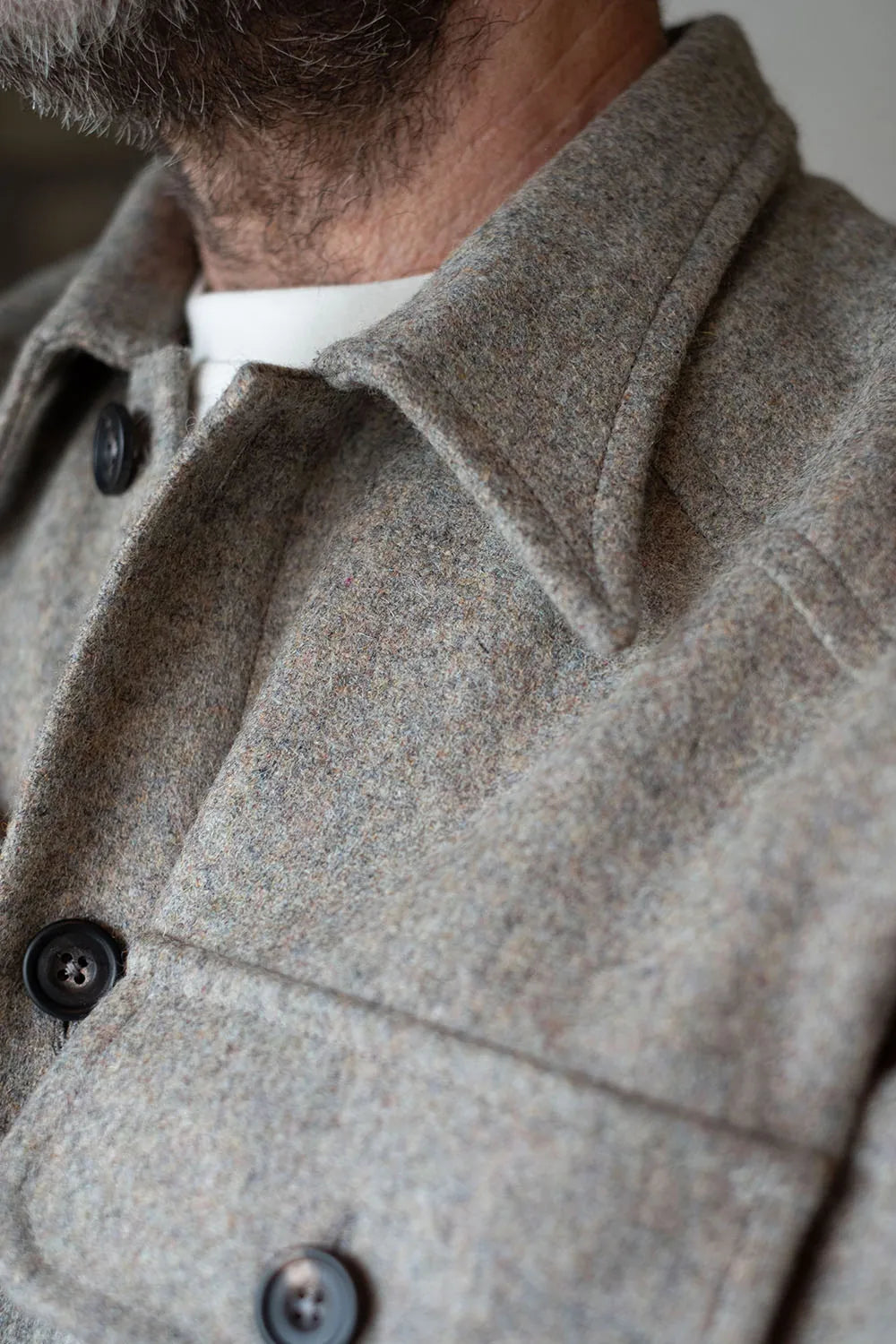 Close-up of a person wearing a textured gray USB37 wool overshirt or jacket with dark buttons over a white shirt.